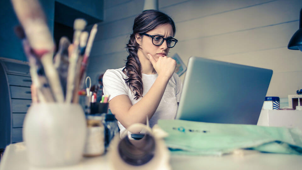 Ein Frau, die vor einem Macbook sitzt und grübelt