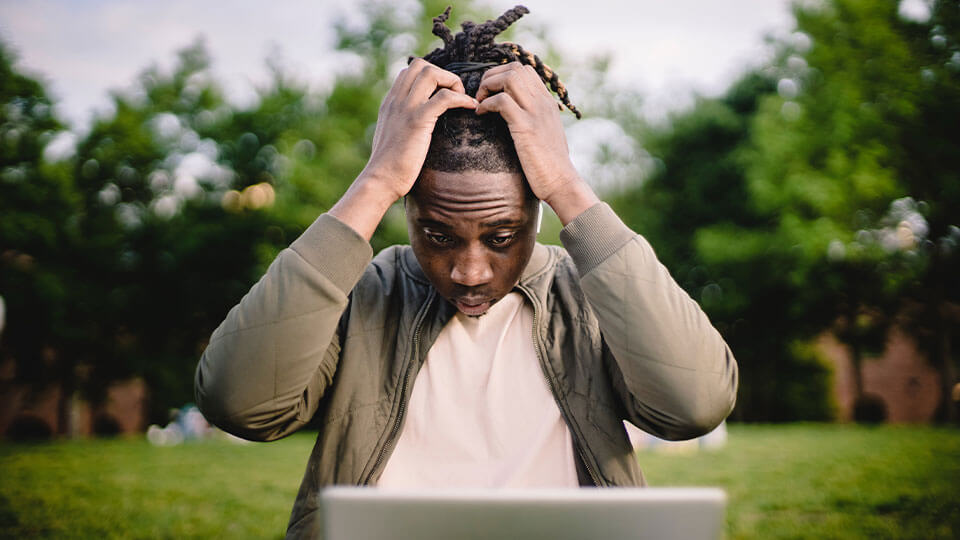 Ein Mann der sich die Haare rauft und dabei vor seinem Macbook sitzt