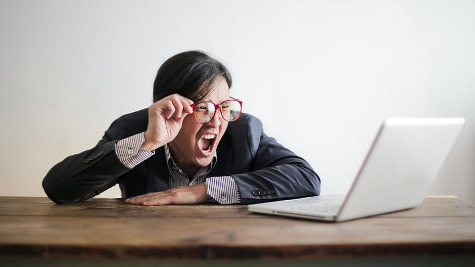 Ein Mann sitzt vor einem Laptop am Tisch und schaut schreit in Richtung Laptop