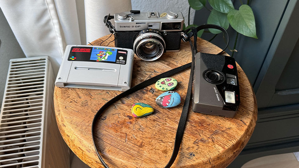 Auf einem Barhocker liegen zwei analoge Kameras und ein paar Pokemon-Steine, so wie ein Super Nintendo Spiel